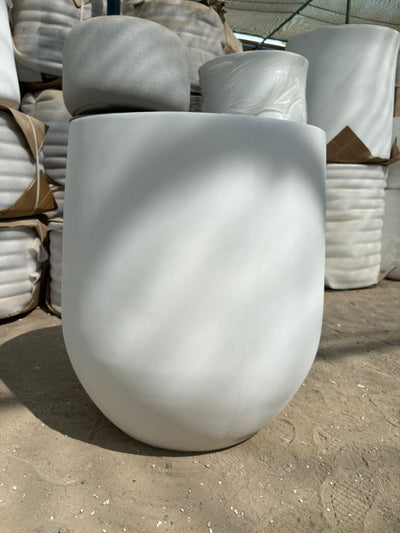 Outdoor and Indoor Large Pot Plant UAE. White concrete planter on a concrete surface with stacks of similar planters in the background.