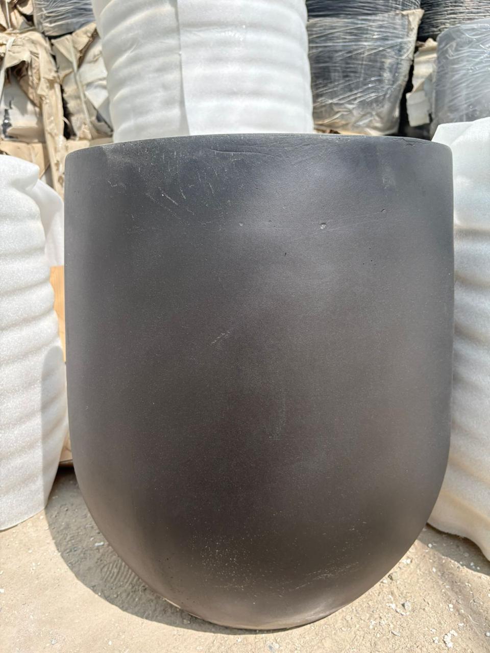 Outdoor and Indoor Large Pot Plant Dubai. Black ceramic pot on a concrete surface with stacked white bags in the background